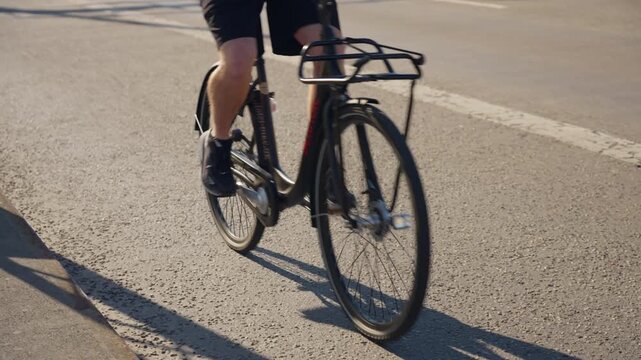 Low-angle close-up captures a cyclist pedaling a red road bike along sunny asphalt, casting sharp shadows while emphasizing fitness, urban mobility, and active lifestyle.