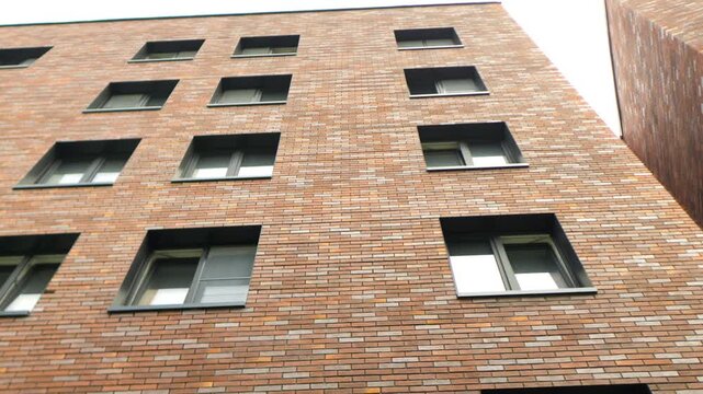 Red brick building dominates the frame. Modern windows feature clean, dark frames. Structured design creates balanced geometry. Angle captures height and depth clearly