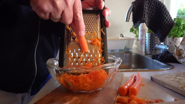 Hirtshals, Denmark A cook grates carrots on a grater by hand  in a residential kitchen. 