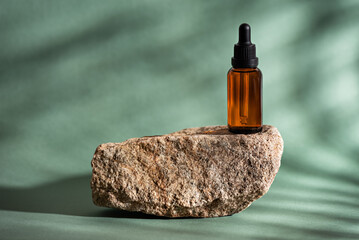 Beauty serum in clear amber glass dropper bottle on stone podium on green background with shadows and light, mockup © Yulia