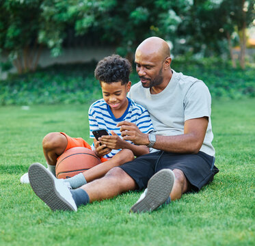 Portrait of father and son having fun using a mobile phone outdoors in park or nature,, family life, parenting, love and bonding concepts