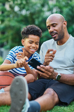 Portrait of father and son having fun using a mobile phone outdoors in park or nature,, family life, parenting, love and bonding concepts