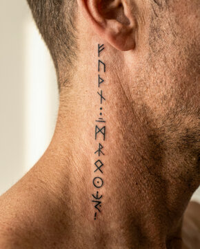 Close-up detail of male skin featuring ancient Viking runic symbols inked behind ear area in minimalist style