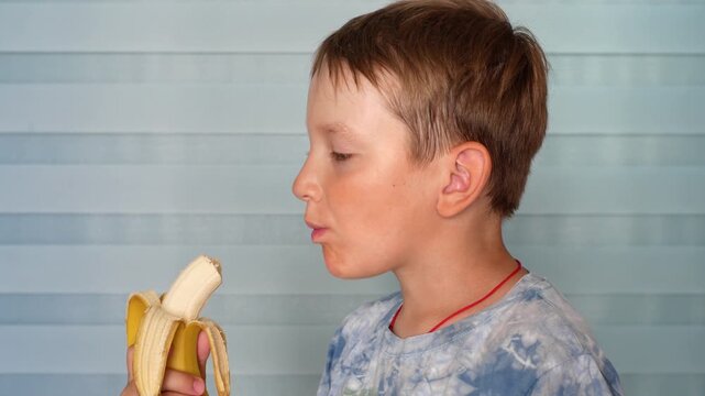 Close-up in profile view of a cute school-age boy eating a fresh organic banana