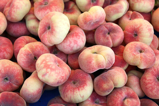 Pile of ripe flat peaches displayed at a local farmers market. Fresh seasonal stone fruit with soft fuzzy skin, natural summer harvest, healthy organic food, agriculture, grocery shopping and farm fre