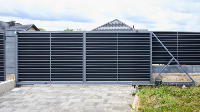 Modern automated cantilever sliding driveway gate featuring anthracite grey horizontal louver slats provides security and privacy for residential property house entrance with paved ground