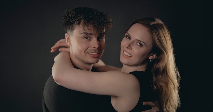 Loving couple hugging, looking at camera and smiling on a dark background