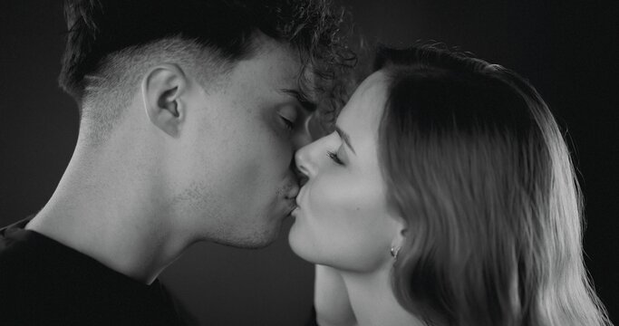Young couple sharing an intimate kiss in a black and white studio
