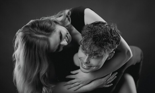 Young couple hugging and laughing on a dark studio background, portraying joy and emotional connection