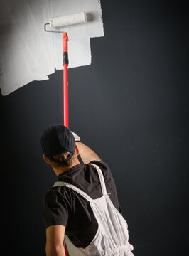 Professional painter painting wall white with long roller during home renovation