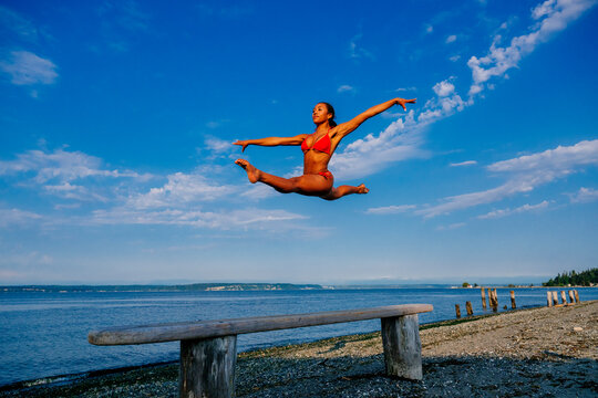 Woman in red swimsuit jumping in a split leap on a beach in WA, USA