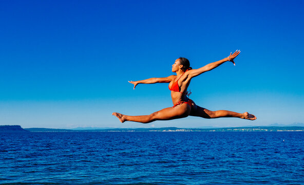 A woman jumps in a red bikini over the ocean on a clear sunny day