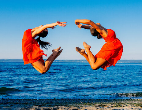 Two women in red dresses perform synchronized jumps at the beach