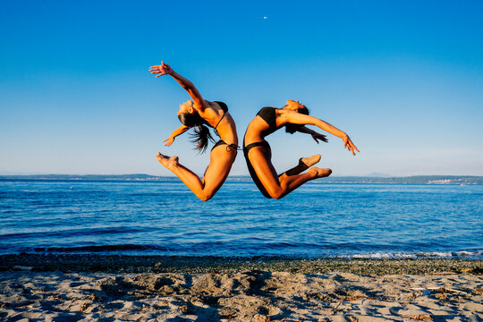 Two women jump in synchronized acrobatic motion on a beach in wa USA