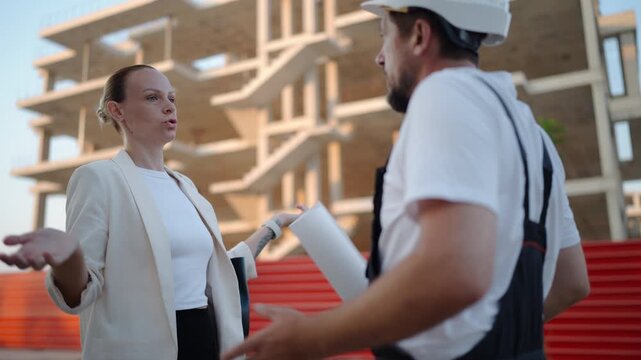 Frustrated female architect arguing with a construction worker holding blueprints at a residential building site, discussing project delays, construction issues and workflow problems.