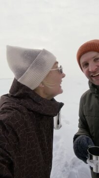 Portrait of young Caucasian couple waving and talking to camera during winter hike in snowy landscape, vertical. Clip is ideal for winter tourism ads or travel vlogging promos