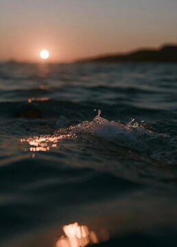 Photograph of the sun setting over the ocean. the sky is a beautiful orange and pink color, with the sun partially visible in the top right corner.