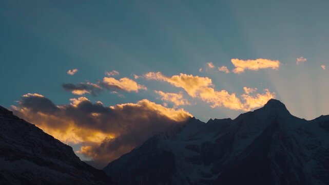 Landscape shot of sun rays above the snow covered Himalayan mountain peaks with orange clouds surrounding it during the autumn season as seen from Keylong in Lahaul Valley, Himachal Pradesh, India.