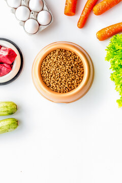 Dry pet food with natural ingredients. Raw meat, vegetables zucchini and carrot near eggs on white backgroud top view copy space