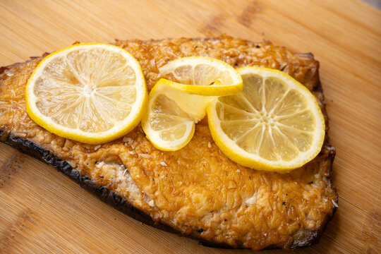 Close-up of golden-baked salmon fillet with fresh lemon slices on a rustic wooden surface with a discreet text area around the dish.
