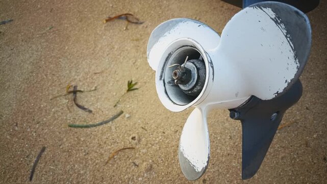 Close up shot of a worn white boat propeller on an outboard motor over sandy terrain.
