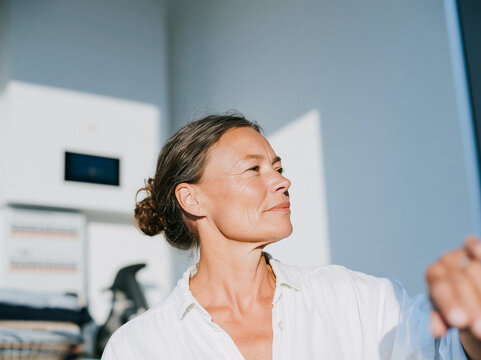 Confident Mature Woman Looking Out Window in Bright Modern Home Interior