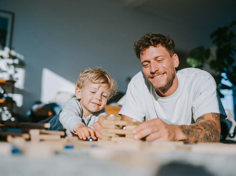 Happy Tattooed Father Laughing with Young Child at Home Dining Table