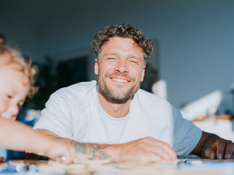 Happy Tattooed Father Laughing with Young Child at Home Dining Table