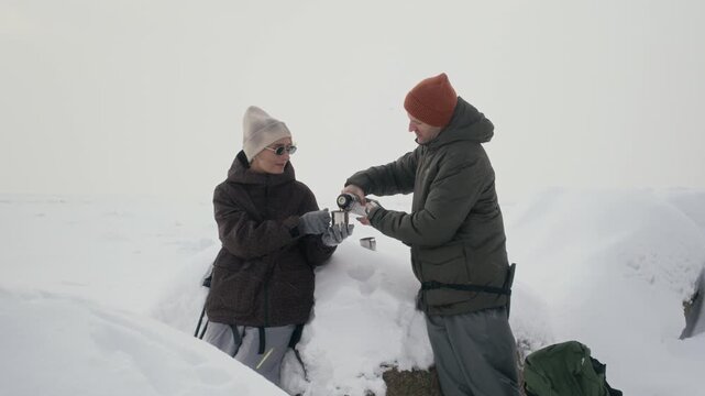 Caucasian couple pouring and drinking hot tea from thermos during winter hike in snow. Footage is perfect for outdoor gear advertising and winter tourism promos
