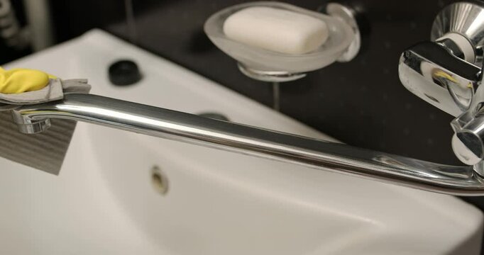 Cleaning the bathroom faucet, hands in yellow gloves wipe the faucet with a cleaning solution.