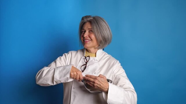 Female chef in uniform mixing ingredients in a stainless steel bowl, looking at camera with confidence and winking on a blue background. Concept for cooking mastery and recipe prep.