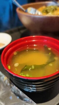 Open lacquered bowl of hot Japanese miso soup with seaweed
