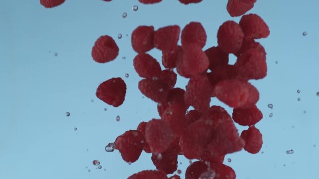 Flying fresh organic red raspberries with water drops in light blue sky