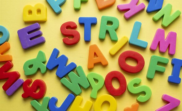 Alphabet letters made of colorful foam scattered randomly across a bright yellow surface to represent early childhood education.
