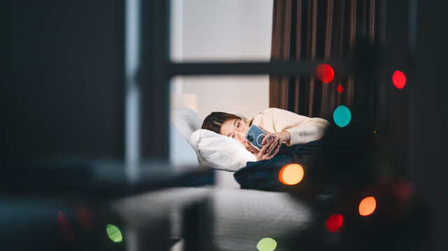 asian woman sleep on bed relaxing at night in bedroom, using smartphone social message or dating app online solitude on Christmas holidyas