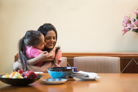 Daughter embracing her mother sitting at dinning table