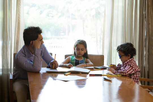Father helping daughter and son with homework