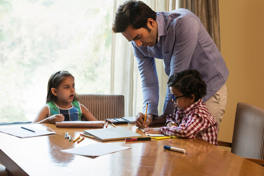 Father helping daughter and son with homework