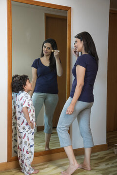Woman applying make-up while her son look on
