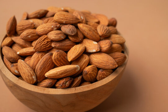 Raw almonds in wooden bowl on brown background highlight protein rich nutrition, wholesome snack choice, protein focused healthy eating, ideal for food marketing, wellness branding, copy space.