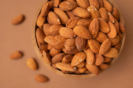 Wooden bowl filled with dry almonds on warm brown background presents healthy food concept, plant based nutrition, natural protein source, organic lifestyle promotion, clean food design.