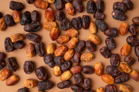 Natural dried dates scattered on warm brown background, varied fruit textures create organic visual appeal. Natural food concept fits packaging, retail promotion, healthy snack advertising 