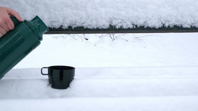 A black thermos mug sits on a snowy surface. The surrounding area is covered in fresh white snow, creating a serene winter scene.