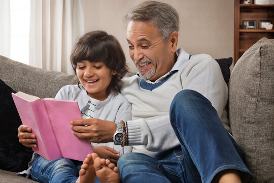 Grandfather and grandson reading book sitting together on sofa