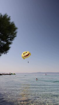 Vertical screen Smiling parasail drifts above crystal clear sea creating a playful summer vacation scene filled with freedom coastal adventure and sunny holiday vibes