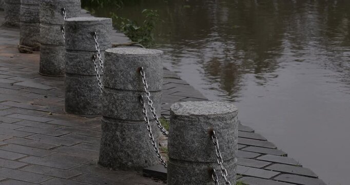 Stone bollards and chain boundary along the edge of a calm river bank