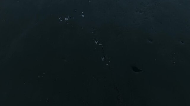 Drone view flying low over partially frozen surface of Lake Sils surrounded by snow capped mountains in Swiss Alps. Aerial forward tilt-up reveal