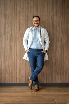 Friendly medical professional smiling, standing confidently against a textured wall, representing trust, expertise, and a welcoming approach to healthcare and wellness services