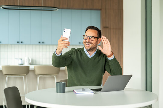 Entrepreneur participating in a video call, communicating with clients, colleagues, or legal counsel using a smartphone and laptop from a modern office setting