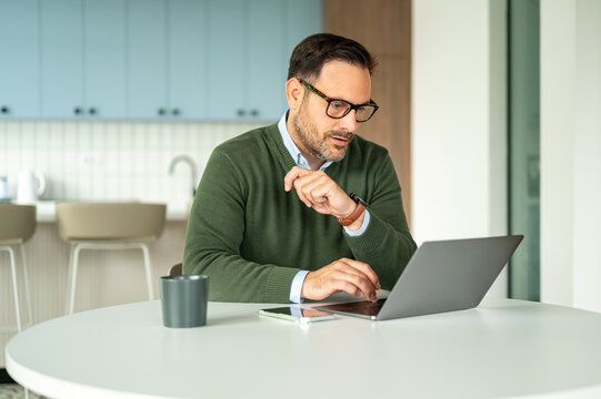Professional man concentrating on his laptop. Managing business finances. Legal work. Or distance education from a contemporary kitchen or home office environment